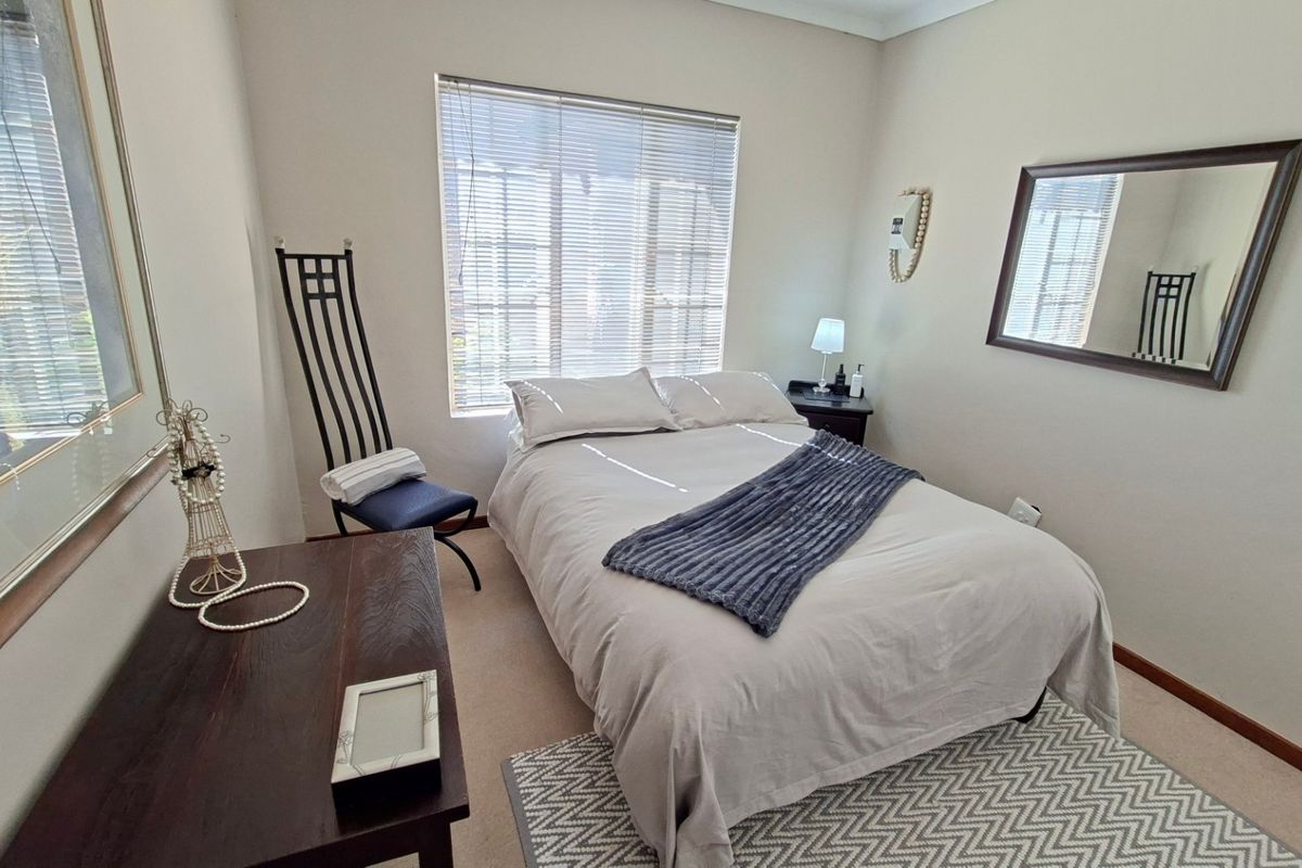 A functional bedroom featuring neutral wall tones, carpeted flooring, and a window fitted with venetian blinds.