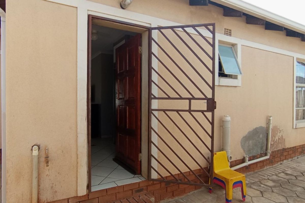 Rear exterior view of the property featuring a security gate, timber entrance door, and visible plaster damage on the exterior wall.