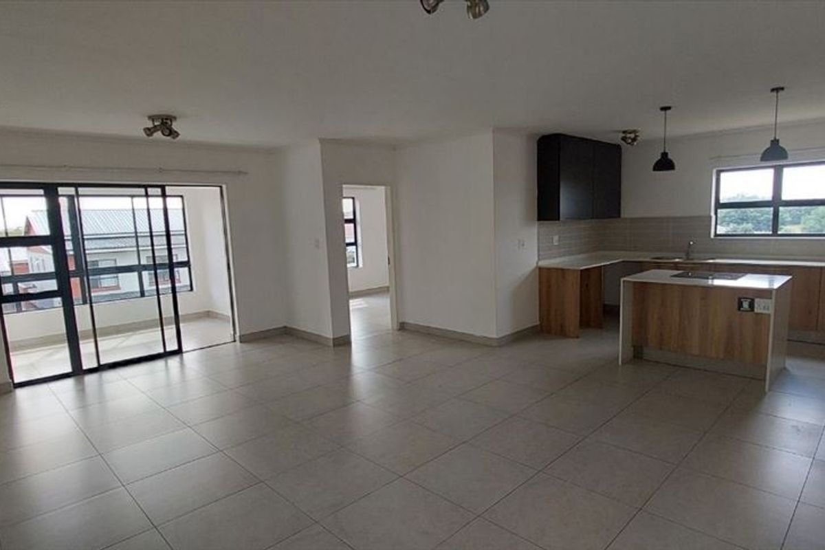 Spacious open-plan living area featuring a modern kitchen with island, tiled flooring, and sliding doors leading to a balcony.