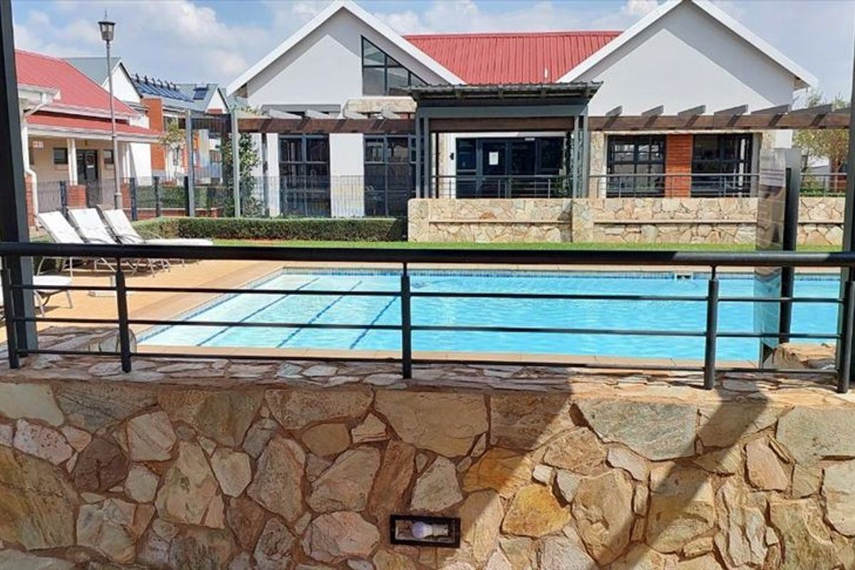 A well-maintained communal swimming pool area featuring stone-clad retaining walls, metal safety railings, and a pergola structure within a townhouse complex.