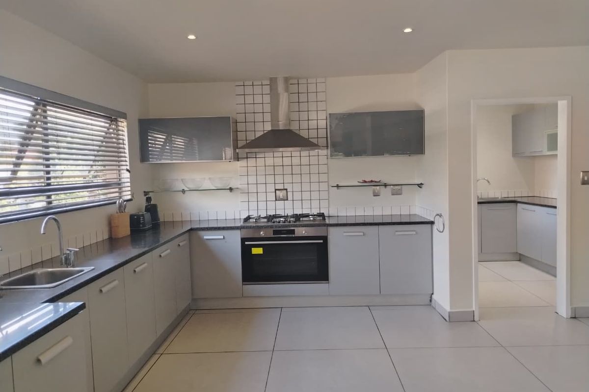 Modern kitchen featuring grey cabinetry, granite countertops, gas hob, extractor fan, and tiled flooring, with an adjacent scullery area.
