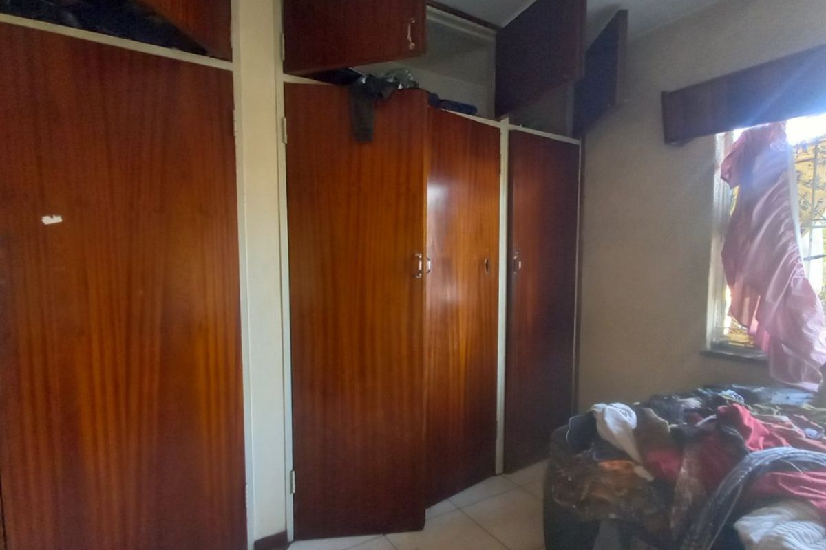 Bedroom featuring built-in wooden cupboards and tiled flooring, requiring cosmetic updates to improve the overall aesthetic and functionality of the storage space.