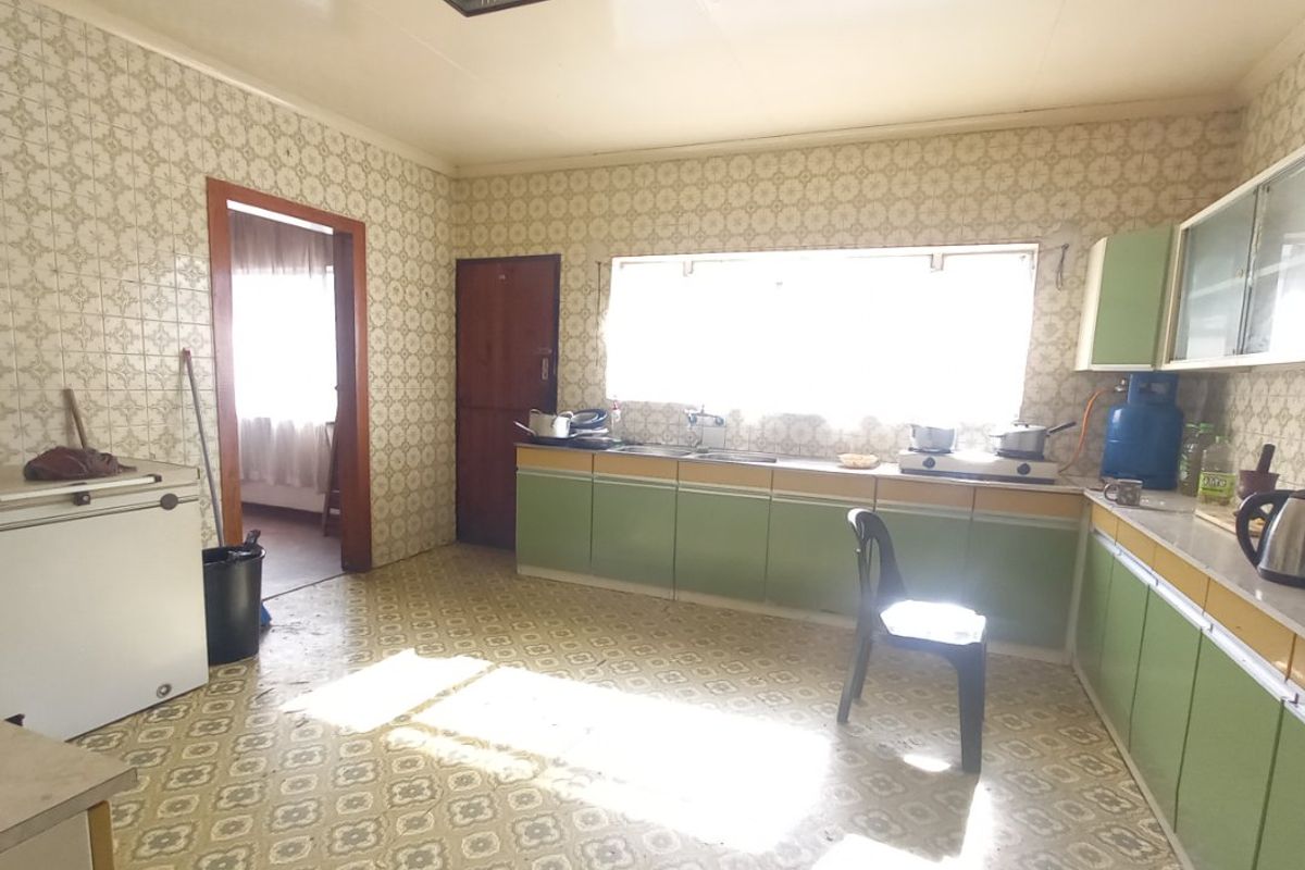 A dated kitchen featuring original cabinetry, tiled splashbacks, and worn vinyl flooring, offering significant potential for a modern renovation.