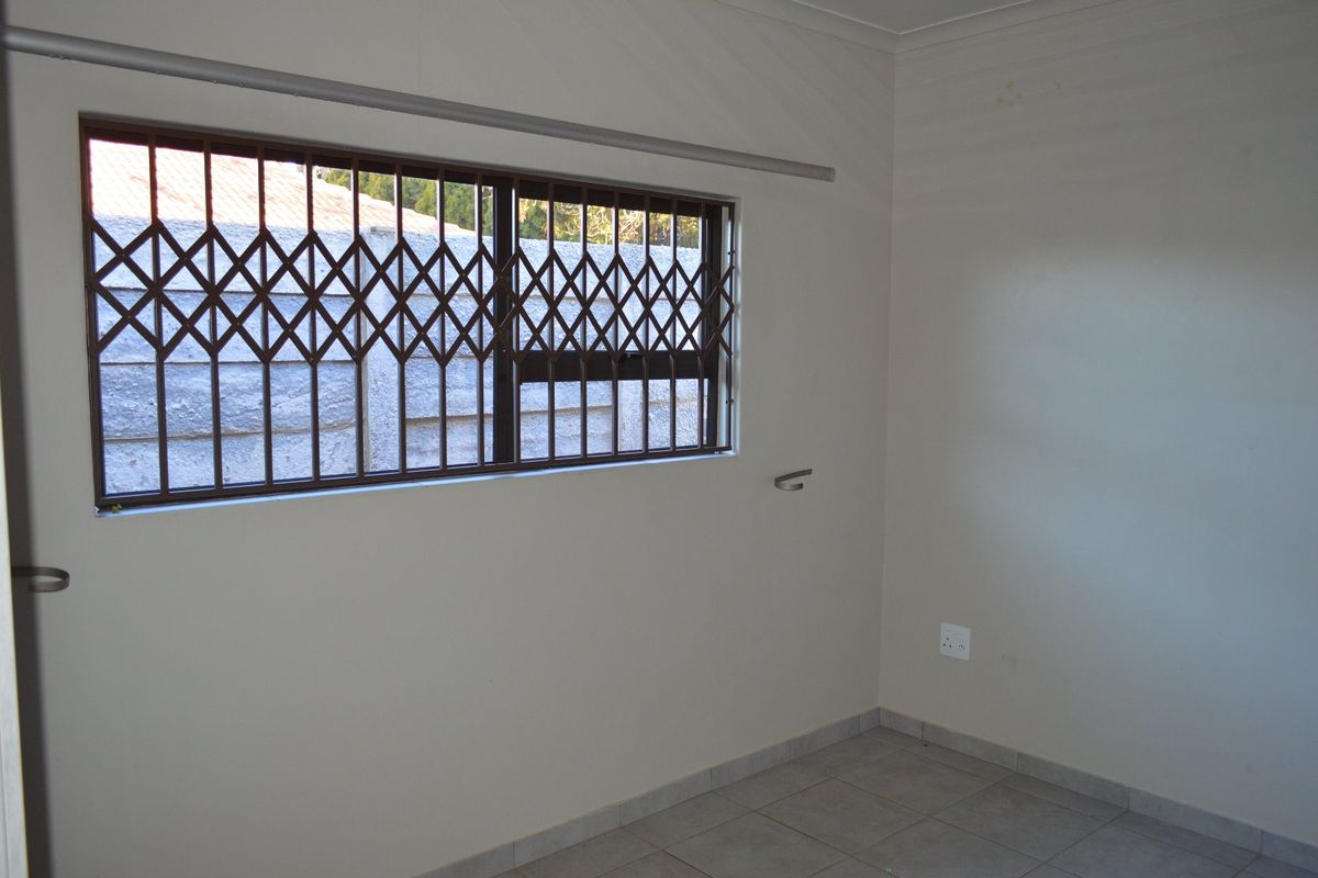 A clean, empty bedroom featuring tiled flooring and a window fitted with a security gate.