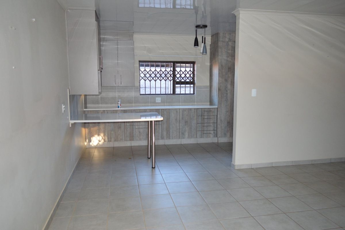 A clean, modern kitchen featuring neutral cabinetry, laminate countertops, a breakfast bar, and tiled flooring, offering a functional and well-maintained space.