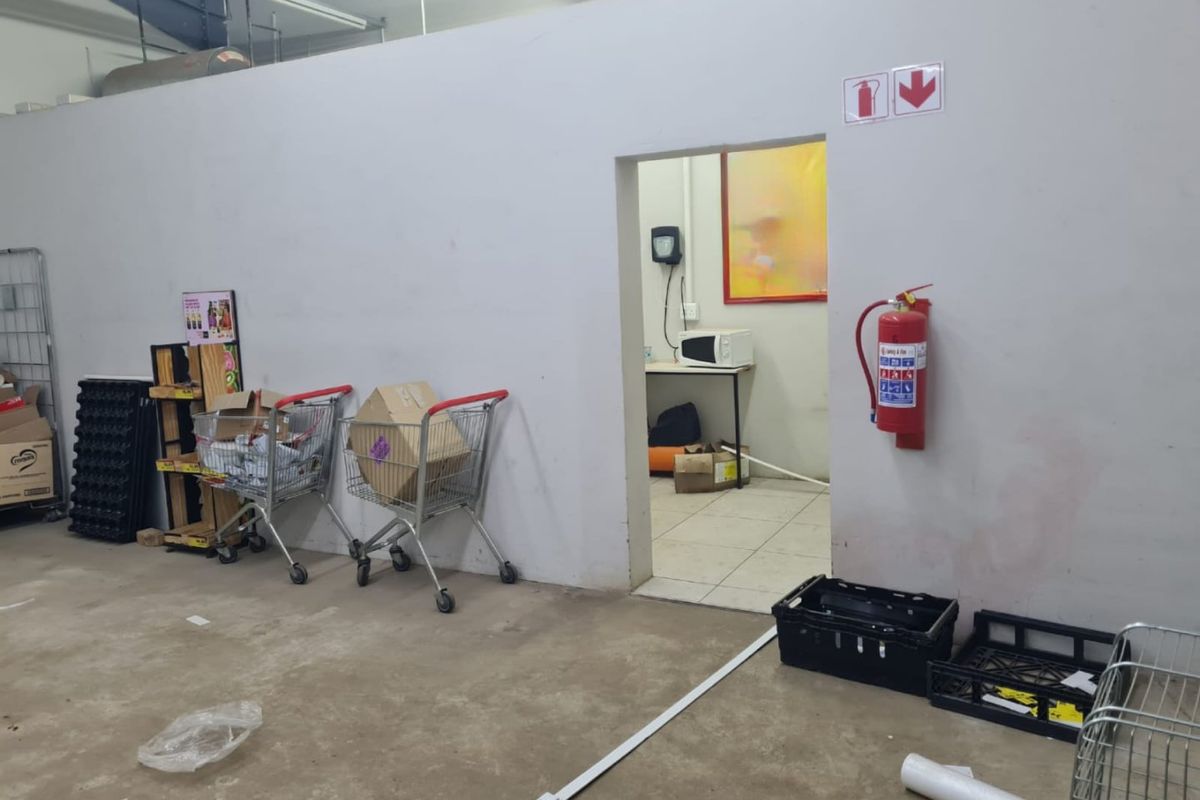 A functional utility or storage area within a commercial space, featuring basic finishes, fire safety equipment, and direct access to an adjacent small room.