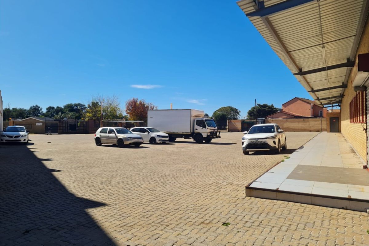 Spacious paved commercial yard area featuring a metal roof canopy and brick building facade, suitable for parking or logistics operations.