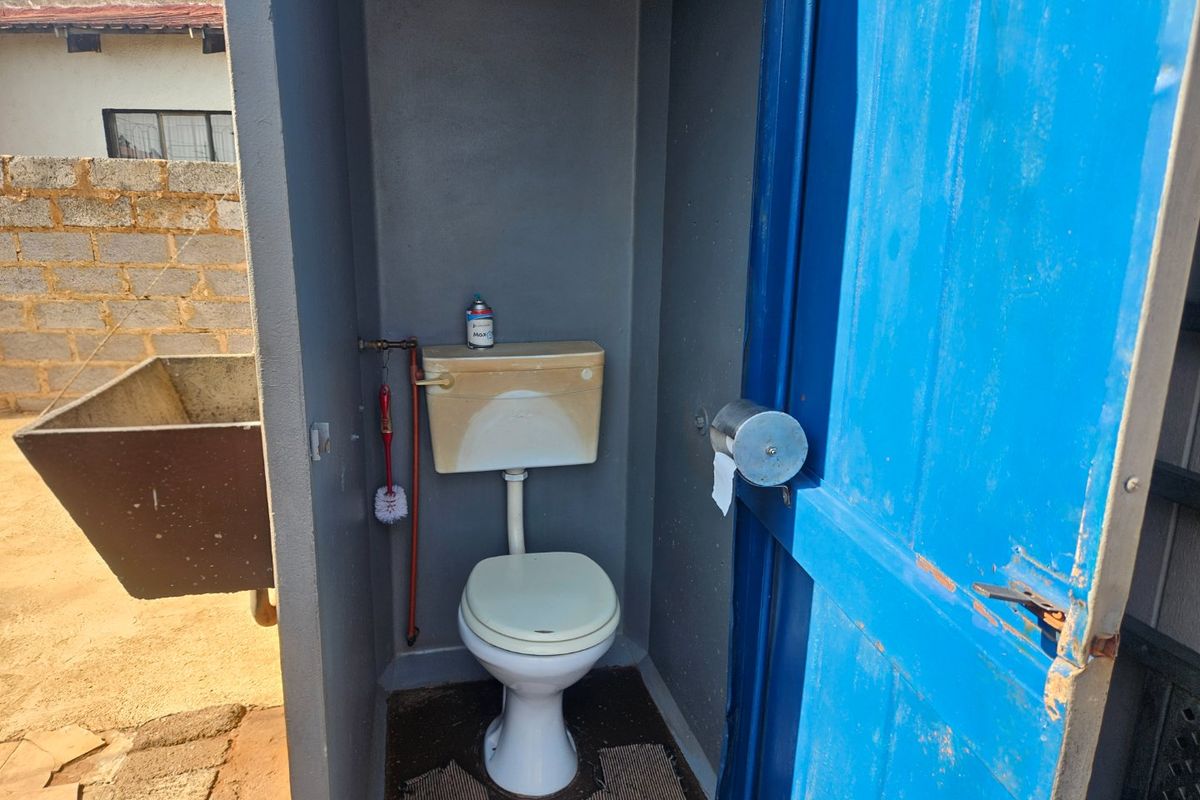 A basic outdoor toilet facility featuring a standard white toilet and cistern, housed within a simple structure with a blue door.