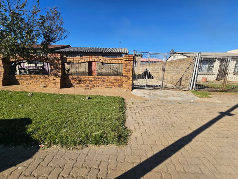 Front view of the property featuring a brick boundary wall, metal security gate, and paved driveway access.
