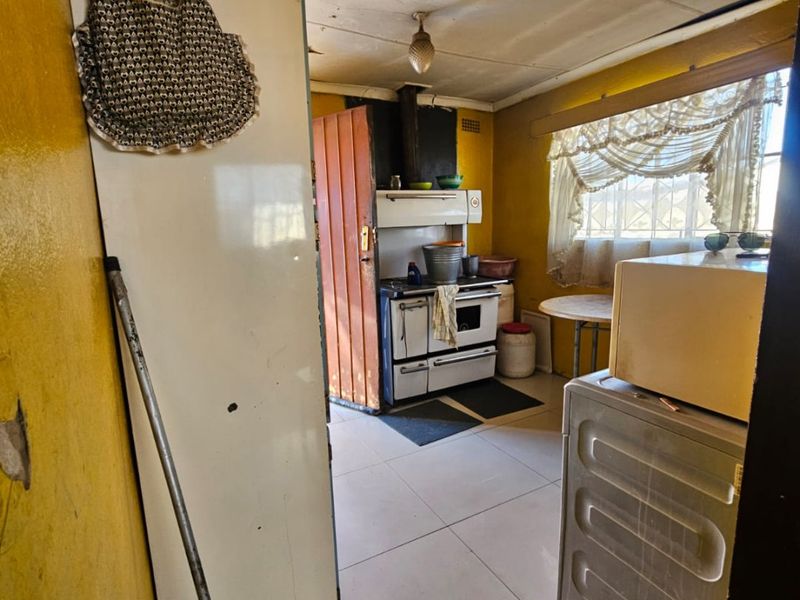 A dated kitchen area featuring tiled flooring and a freestanding stove, requiring significant cosmetic updates and refurbishment to improve its overall condition and functionality.