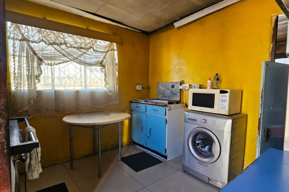 A dated kitchen area featuring tiled floors, basic cabinetry, and a window with security bars, requiring significant cosmetic updates and renovation.