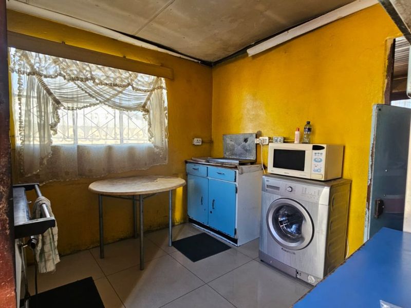 A dated kitchen area featuring tiled floors, basic cabinetry, and a window with security bars, requiring significant cosmetic updates and renovation.