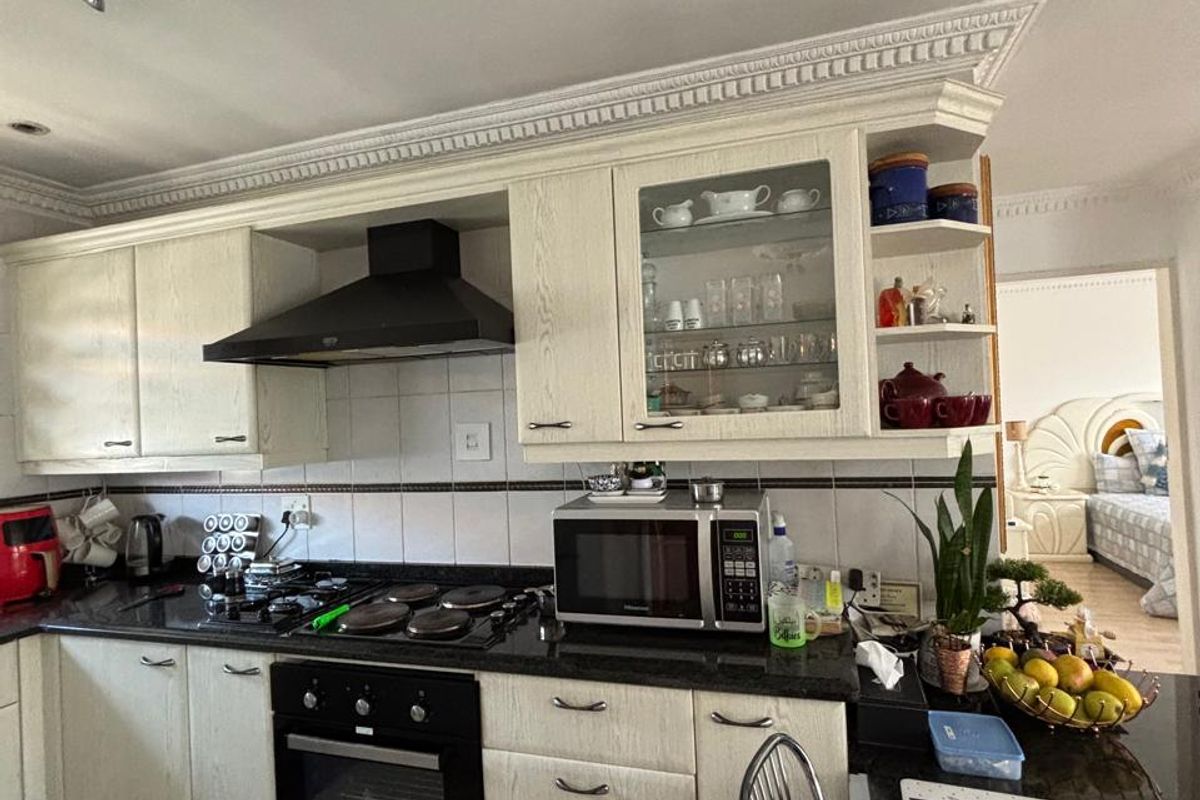 A functional kitchen featuring cream cabinetry, granite countertops, a built-in oven, and a decorative ceiling cornice, with an adjacent view into the bedroom.