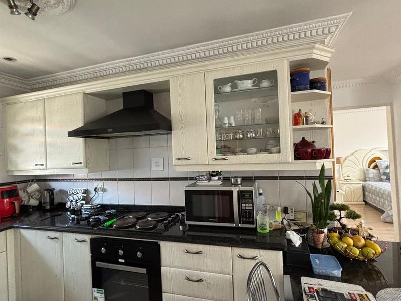 A functional kitchen featuring cream cabinetry, granite countertops, a built-in oven, and a decorative ceiling cornice, with an adjacent view into the bedroom.