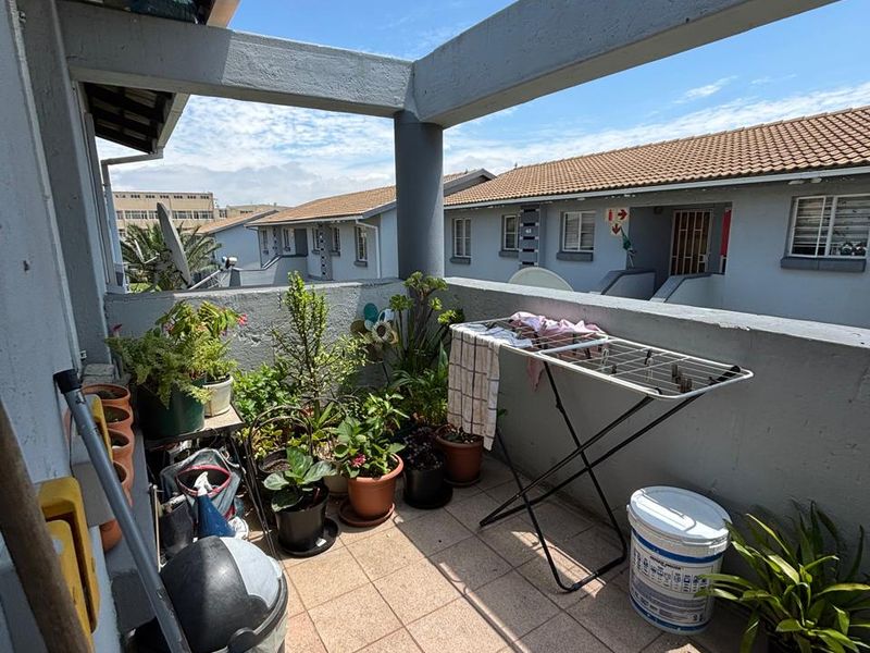 A functional balcony area featuring tiled flooring and a concrete balustrade, offering an open-air space with views of the surrounding apartment complex.