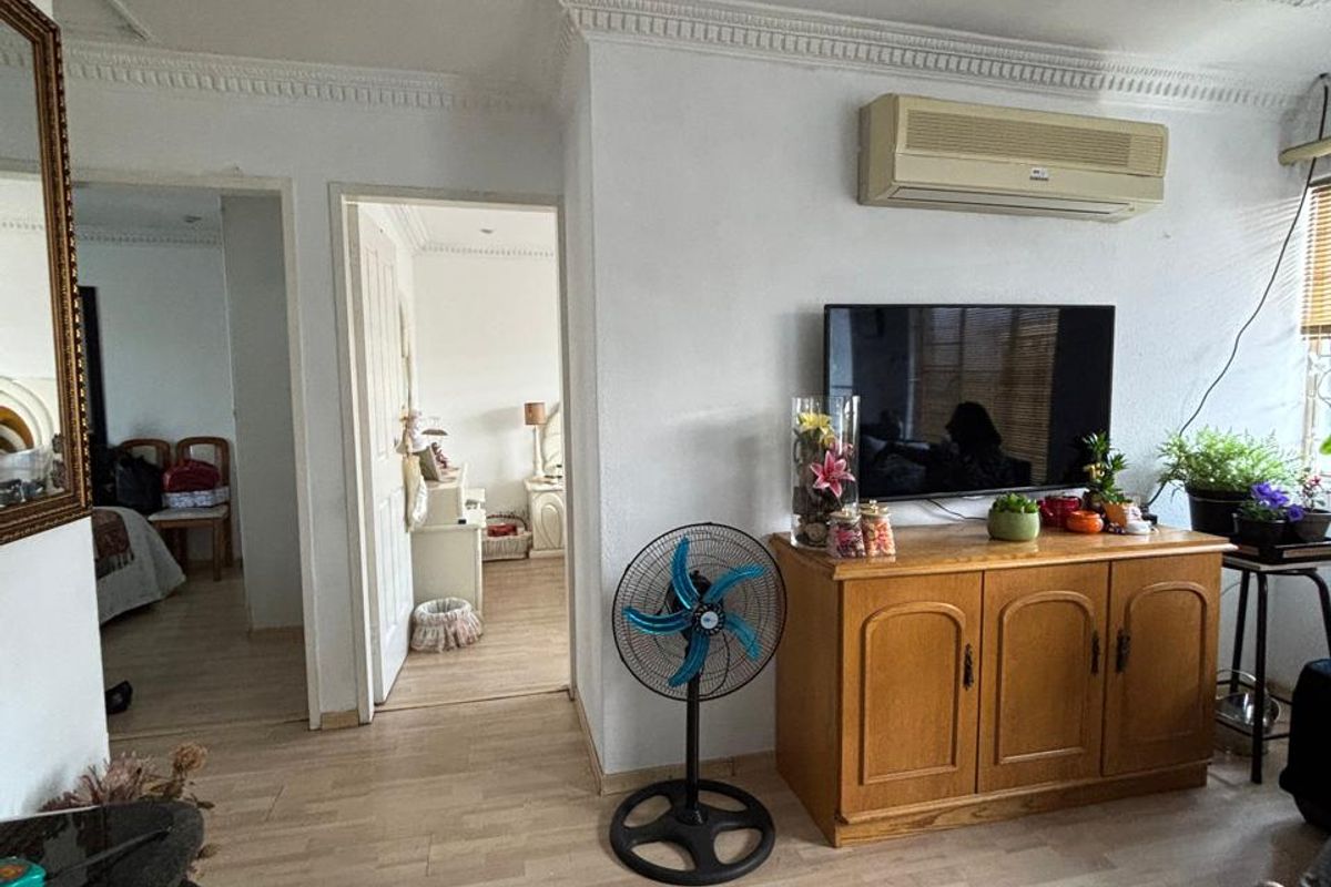 Living room featuring laminate flooring, decorative ceiling cornices, and a wall-mounted air conditioning unit, providing access to adjacent rooms.
