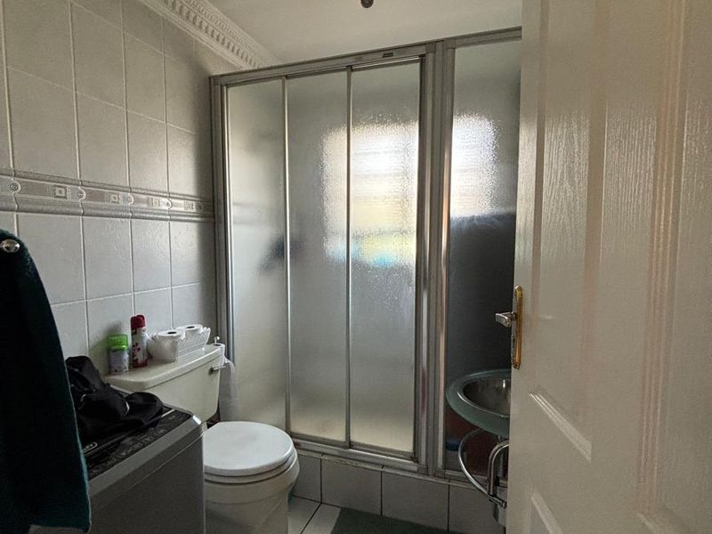 A compact bathroom featuring a shower enclosure, toilet, and pedestal sink with tiled finishes and decorative ceiling detailing.