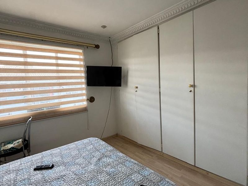 A bedroom featuring laminate flooring, built-in cupboards, and decorative ceiling cornicing, providing a functional and neutral living space.