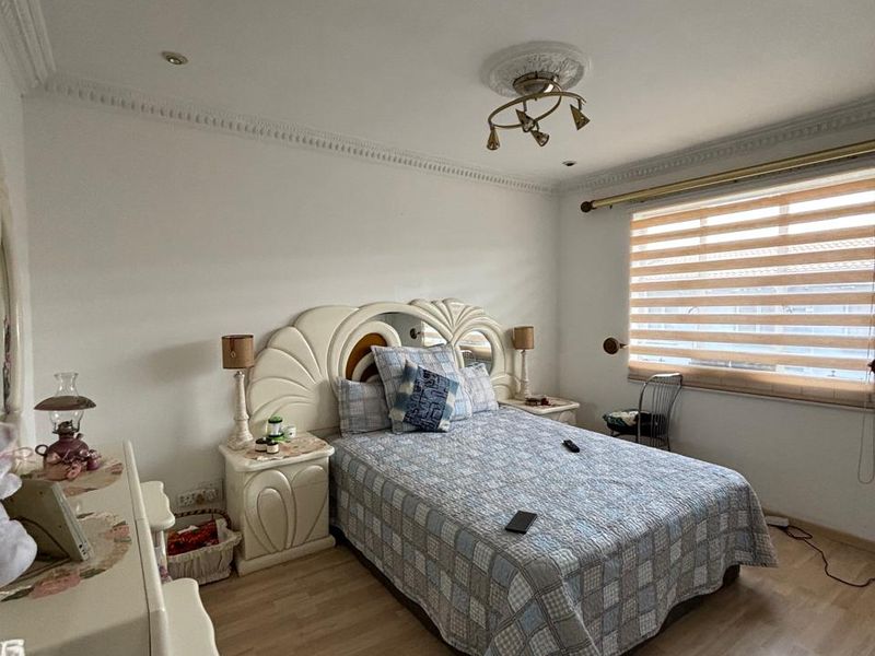 A well-lit bedroom featuring laminate flooring, decorative ceiling cornice, a central ceiling rose, and adjustable venetian blinds for privacy.