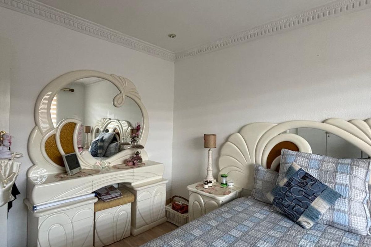 A bedroom featuring decorative ceiling cornicing, a central ceiling rose, and light-toned laminate flooring.