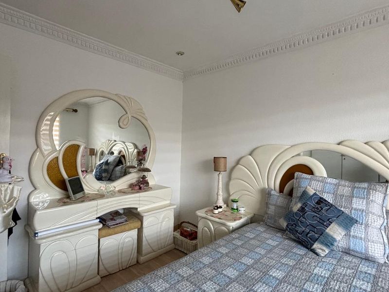 A bedroom featuring decorative ceiling cornicing, a central ceiling rose, and light-toned laminate flooring.