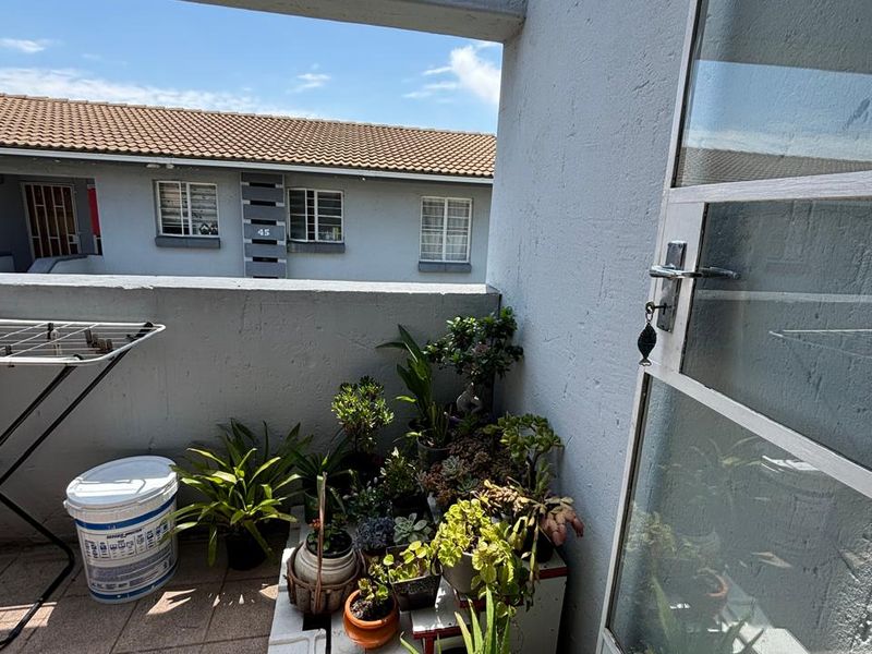 A compact balcony area featuring tiled flooring and a concrete balustrade, offering an outdoor space accessible through a glass panel door.