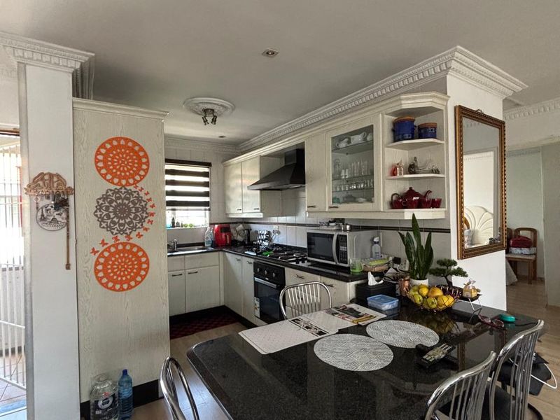 Open-plan kitchen and dining area featuring white cabinetry, dark countertops, integrated appliances, and decorative crown molding.