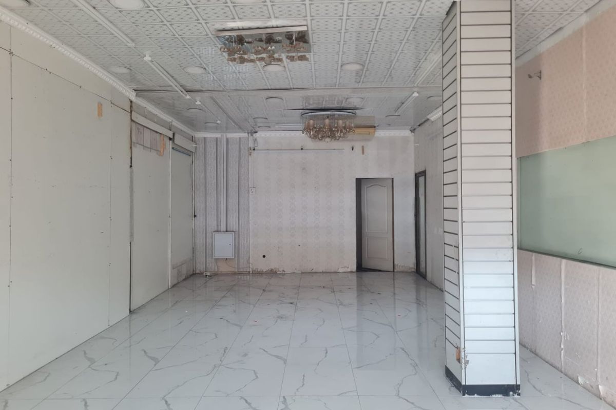 An empty, open-plan interior space featuring marble-look tiled flooring, a decorative drop ceiling with chandeliers, and a prominent structural column.