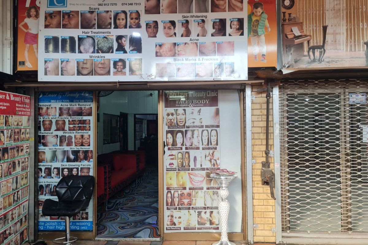 Commercial storefront entrance featuring a brick facade and security gate, currently utilized as a beauty clinic with extensive exterior signage.