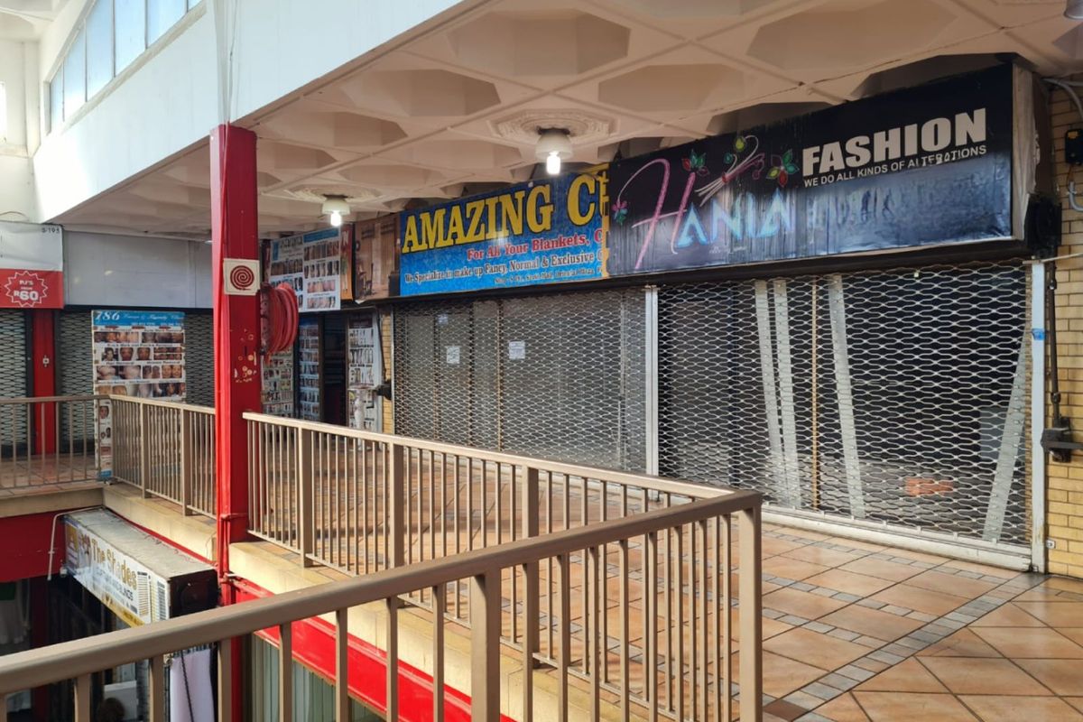 A commercial walkway area featuring metal security shutters, tiled flooring, and a coffered ceiling within a multi-level building complex.