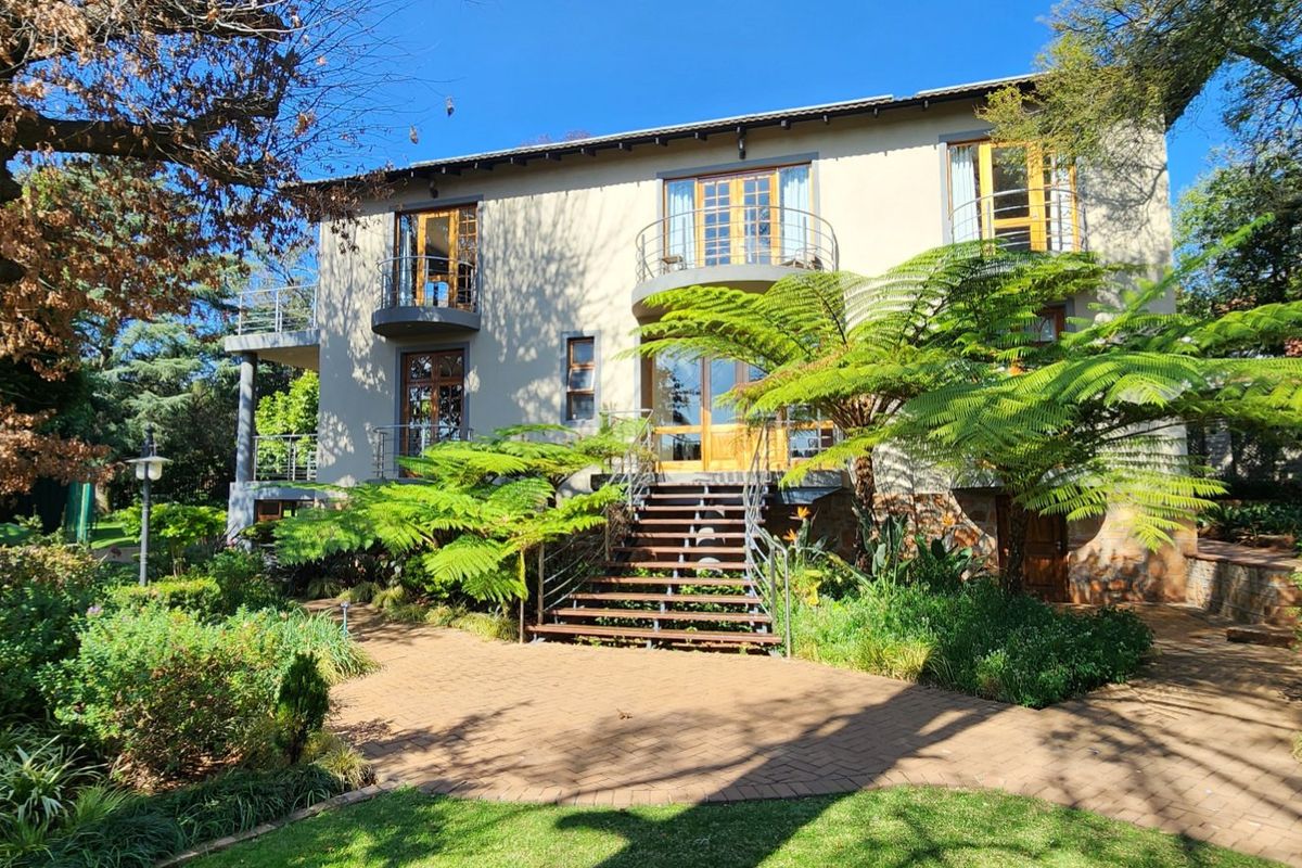 Rear elevation of a multi-story house featuring a paved patio, metal staircase access, and balconies with established garden landscaping.