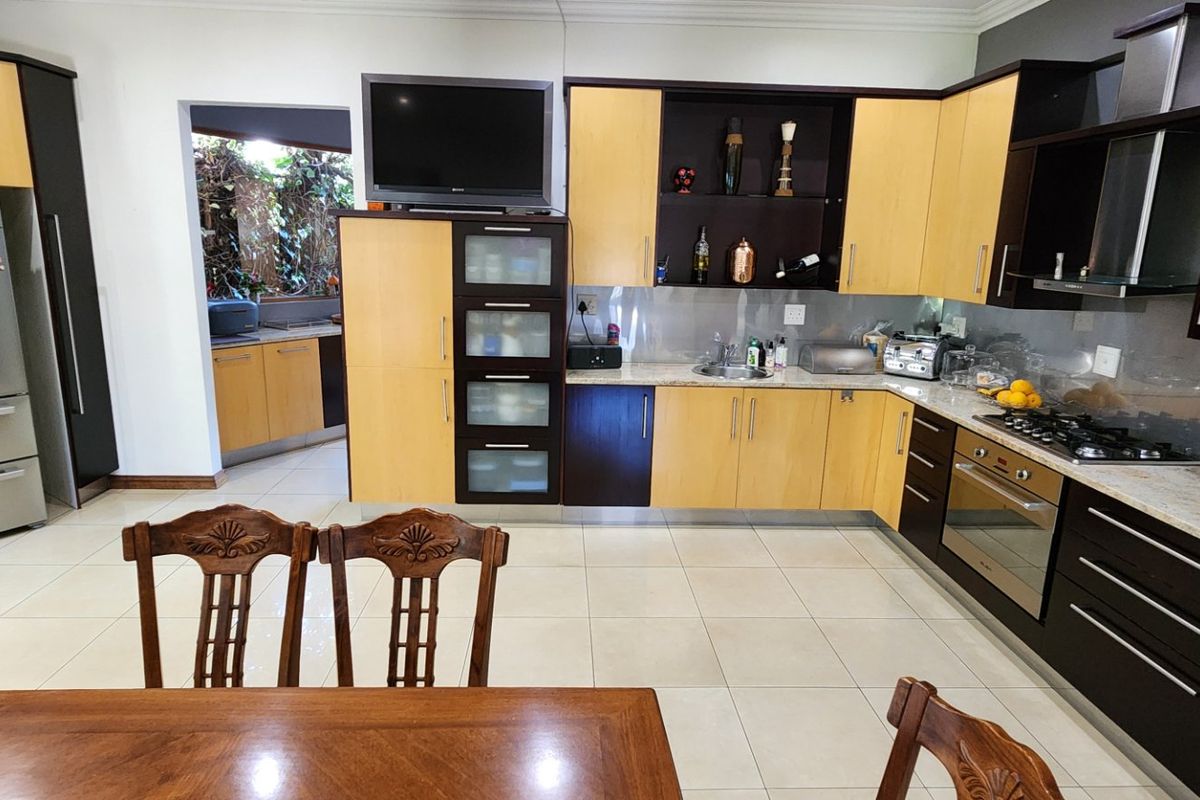 A spacious kitchen featuring two-tone cabinetry, stone countertops, integrated appliances, and tiled flooring, with an adjacent scullery area visible.