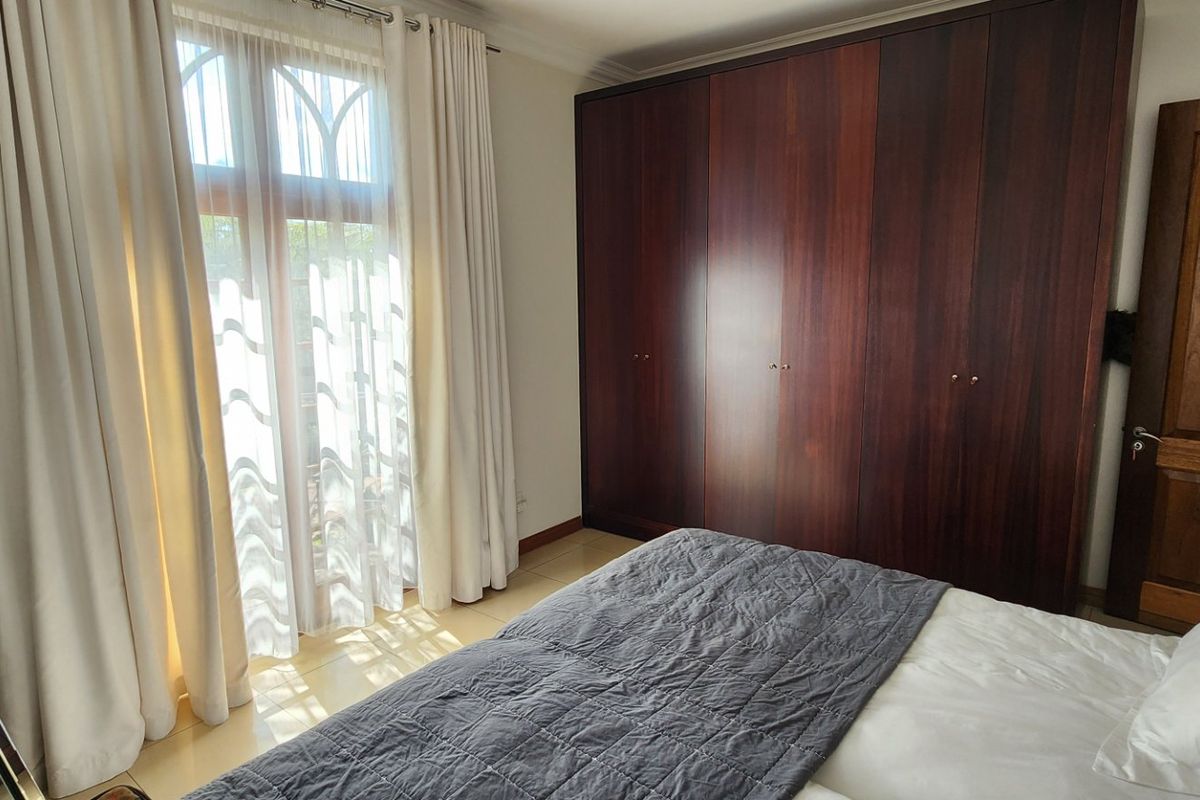 A well-maintained bedroom featuring dark wood built-in cupboards, tiled flooring, and a large window with natural light.