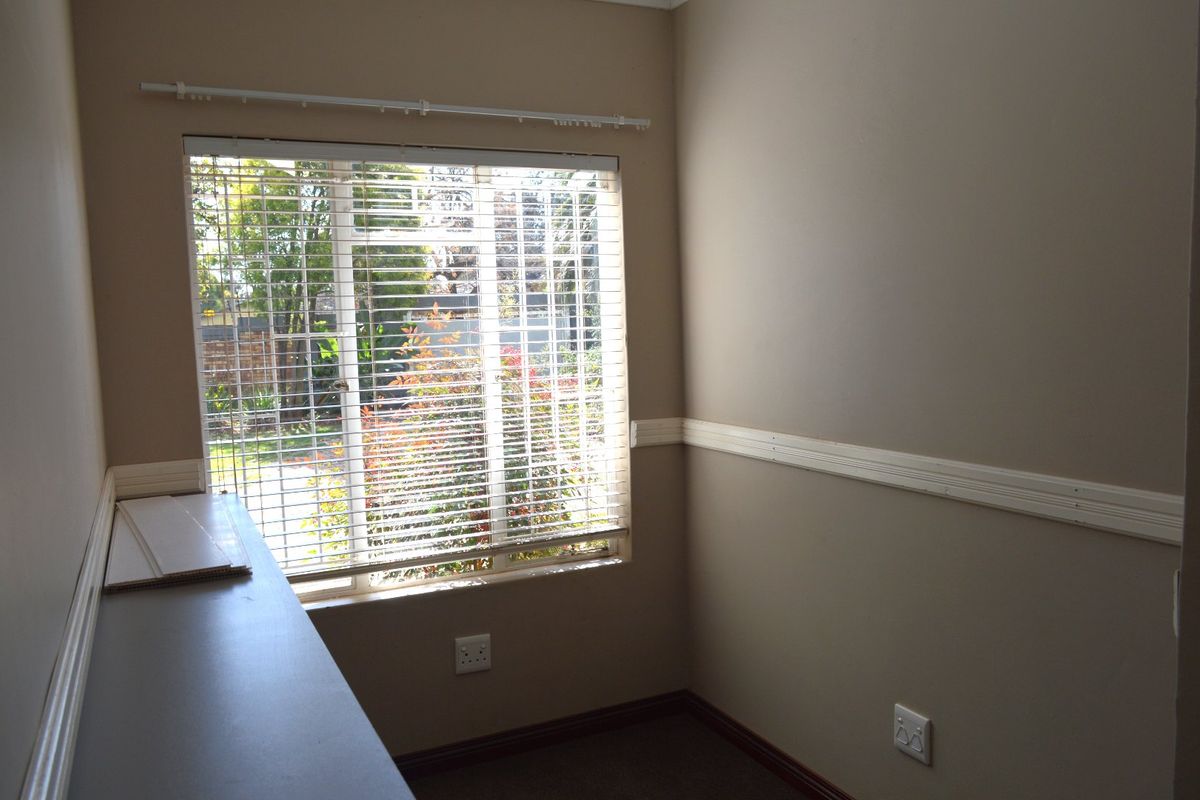 A vacant bedroom featuring neutral wall paint, chair rail molding, a built-in desk, and venetian blinds overlooking the garden.