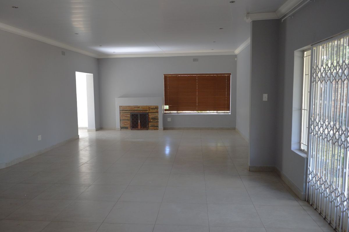 Spacious, empty living room featuring neutral tiled flooring, a built-in fireplace, and large windows with security gates and venetian blinds.