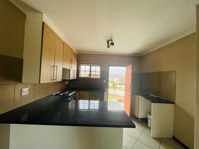 A functional kitchen featuring granite countertops, built-in cabinetry, an electric hob, and tiled flooring, with direct access to an outdoor balcony area.