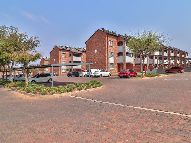 Exterior view of a multi-story brick apartment complex featuring covered parking bays and paved driveway access.