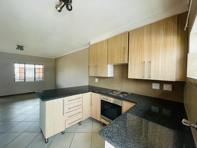 Open-plan kitchen featuring light wood-finish cabinetry, dark granite countertops, and integrated oven and hob, flowing into an adjacent living area with tiled flooring.