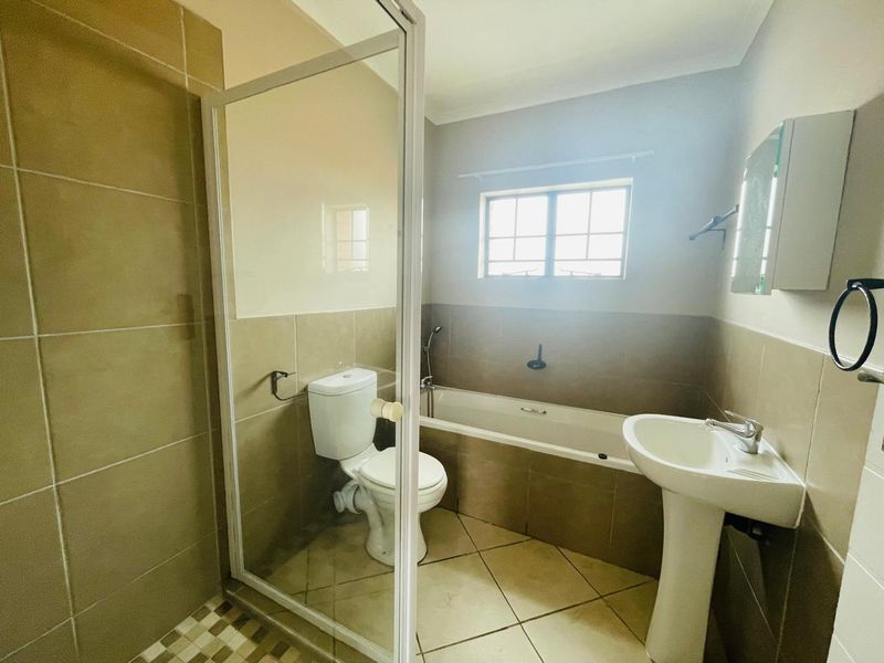 A functional bathroom featuring a pedestal basin, toilet, bathtub, and a separate shower enclosure with neutral wall and floor tiling.