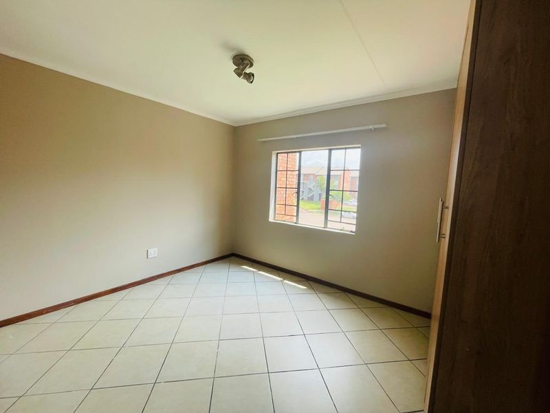 A clean, empty bedroom featuring tiled flooring, a built-in cupboard, and a window with security bars, offering a neutral canvas for personalization.