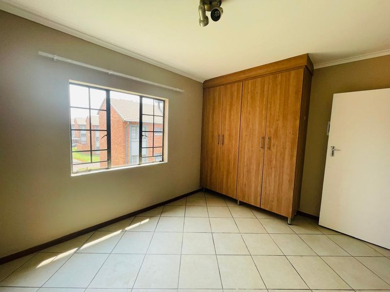 A bright, empty bedroom featuring tiled flooring, a built-in wooden wardrobe, and a window with security bars.
