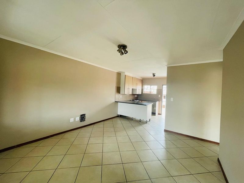 An open-plan living and kitchen area featuring tiled flooring, neutral walls, and functional kitchen cabinetry with a breakfast island.