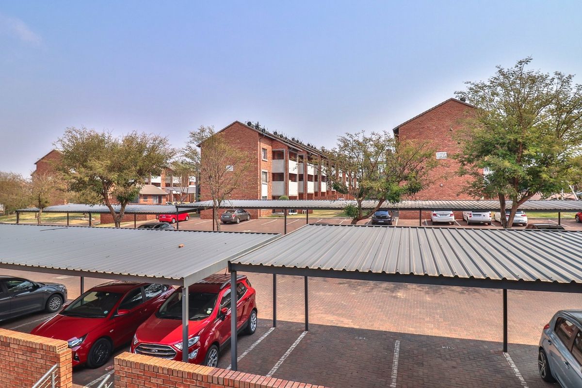View of the apartment complex parking area featuring covered carports and brick paved driveways.