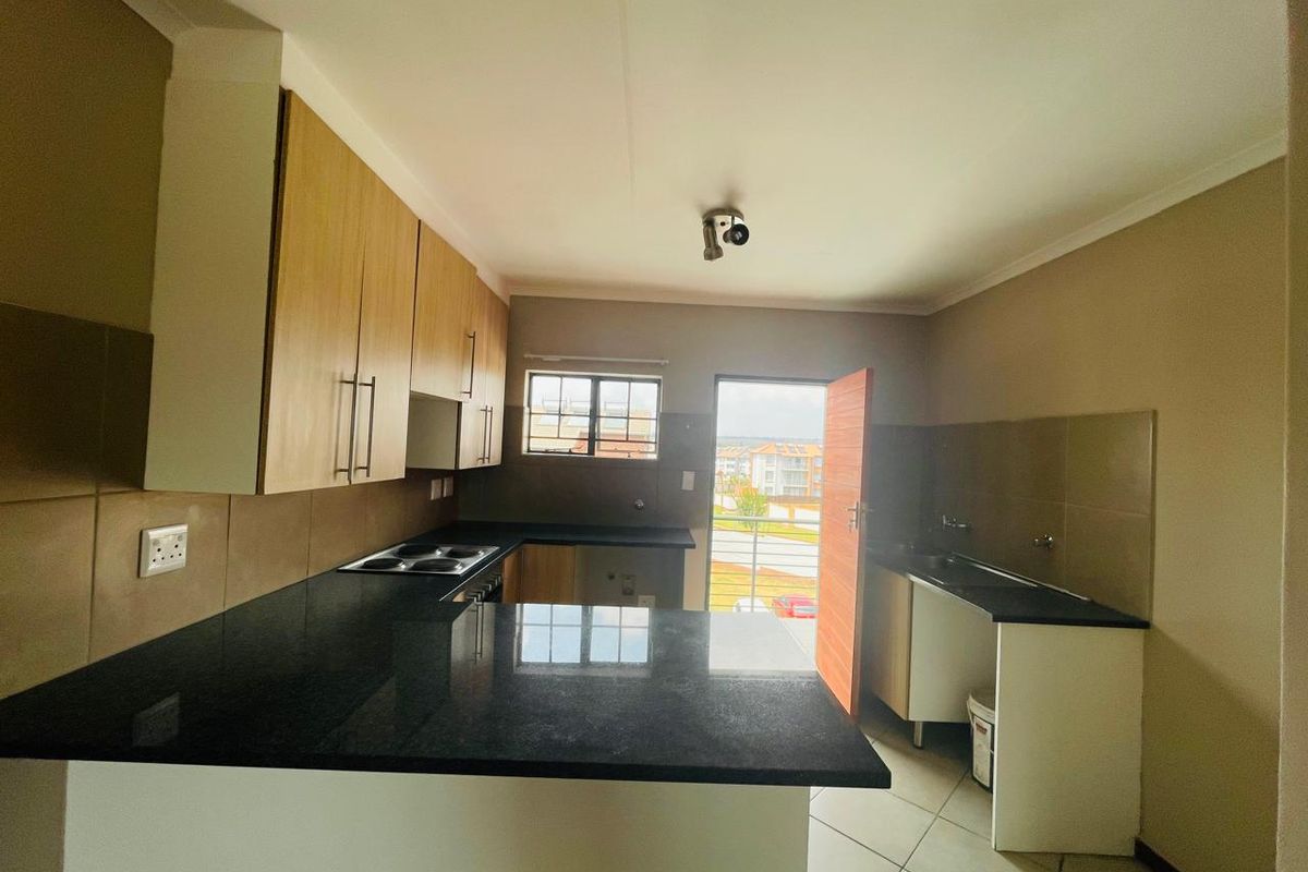 A functional kitchen featuring granite countertops, built-in cabinetry, an electric hob, and tiled flooring, with direct access to an outdoor balcony area.