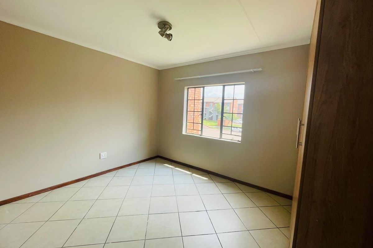 A clean, empty bedroom featuring tiled flooring, a built-in cupboard, and a window with security bars, offering a neutral canvas for personalization.