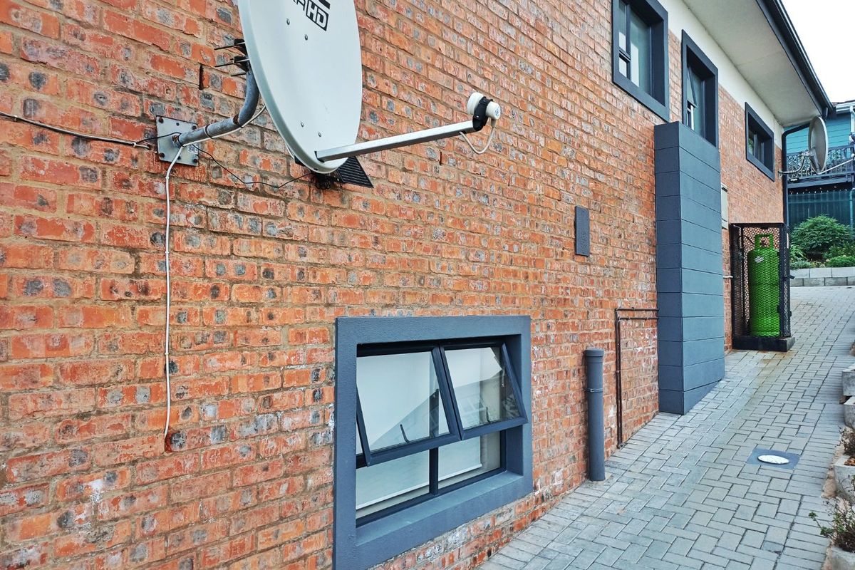 Side view of the property featuring an exposed brick facade, paved walkway, and secure gas cylinder storage area.