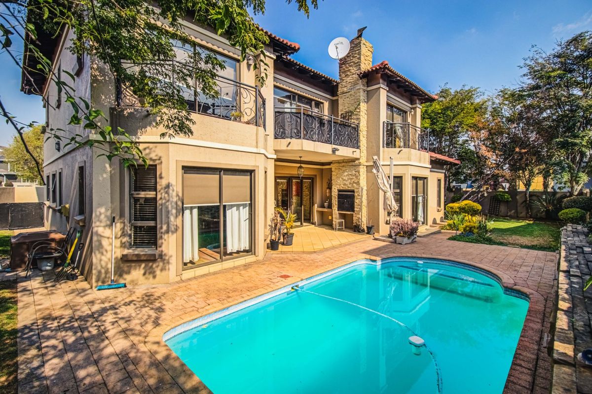 Rear exterior view featuring a swimming pool, paved patio area, built-in braai, and a double-story facade with balconies.