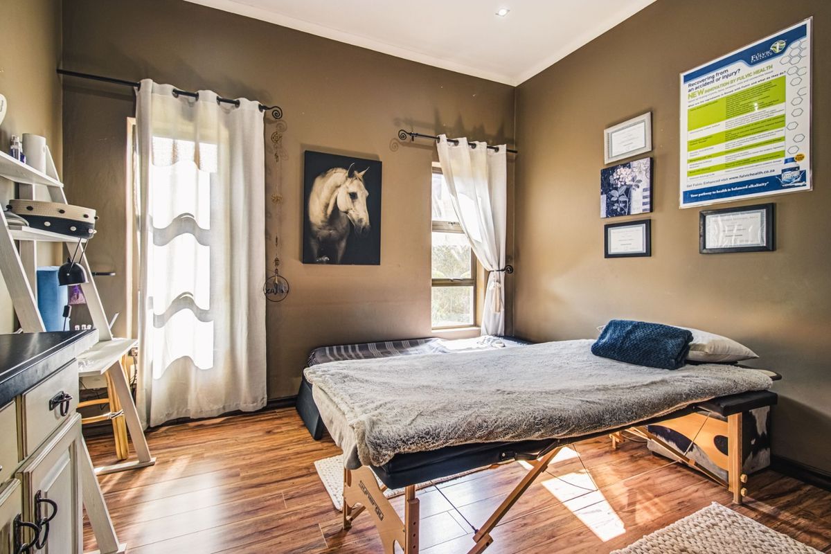 A bedroom featuring laminate flooring and recessed downlights, currently utilized as a treatment room with natural light from the windows.