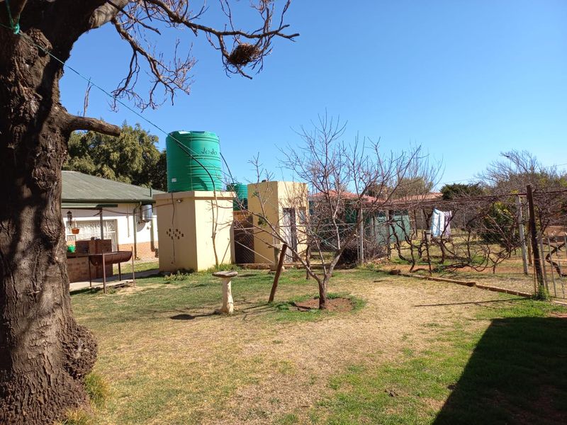 A spacious backyard garden featuring a water storage tank, a brick braai area, and established trellis structures for climbing plants.