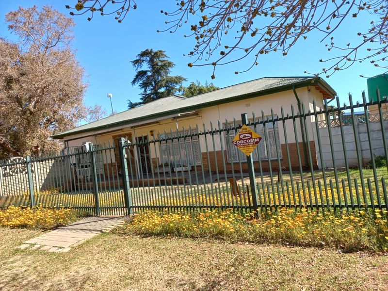 Front view of a single-story house featuring a secure metal fence, gated entrance, and a paved walkway leading to the main entrance.